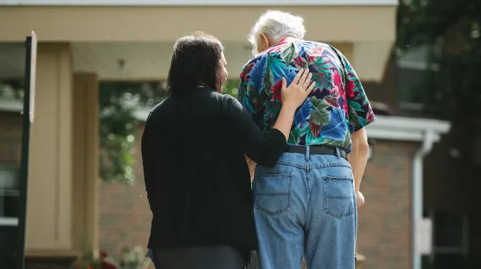 A female provider walking next to a senior male outside of his assisted living community